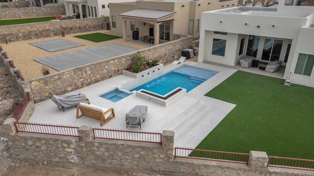Aerial view of a modern backyard with a custom rectangular pool, raised spa, fire feature, and turf lawn designed by Eraland’s Custom Pools in El Paso, TX.