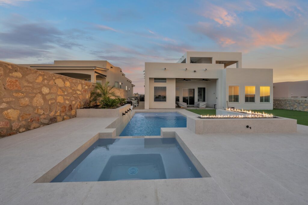 Evening view of a custom pool and raised spa with a linear fire feature, highlighting modern outdoor living by Eraland’s Custom Pools in El Paso, TX.