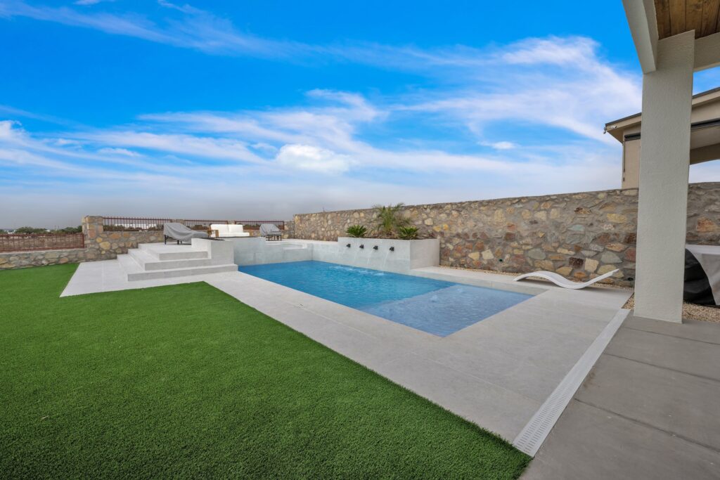 Angled view of the pool with wide entry steps, surrounding turf, and stone privacy wall at a custom Eraland’s Custom Pools installation in El Paso, TX.